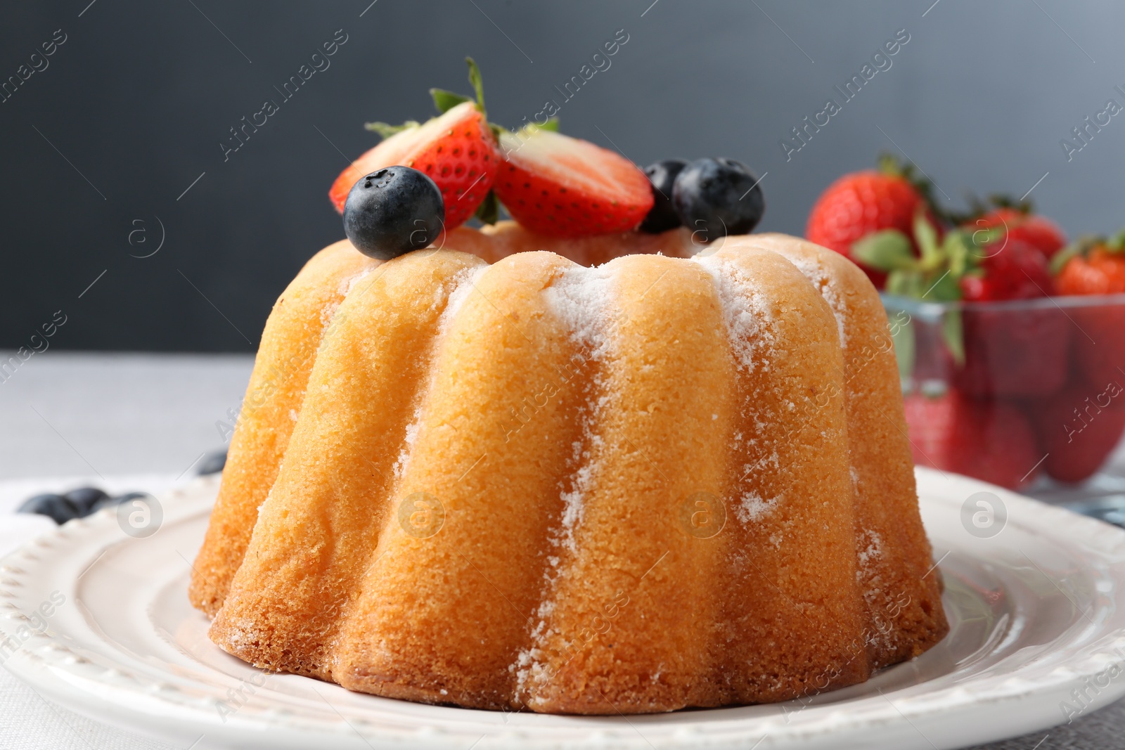 Tasty Bundt cake with powdered sugar and berries on light grey table, closeup Photo of Tasty Bundt cake with powdered sugar and berries on light grey table, closeup