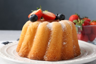 Photo of Tasty Bundt cake with powdered sugar and berries on light grey table, closeup