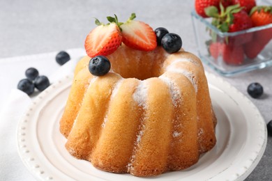 Photo of Tasty Bundt cake with powdered sugar and berries on light grey table, closeup