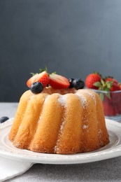Photo of Tasty Bundt cake with powdered sugar and berries on light grey table, closeup. Space for text