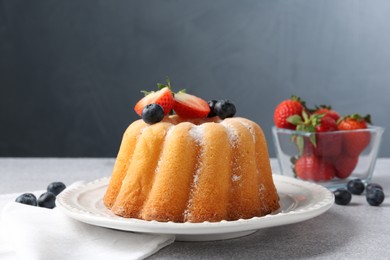 Photo of Tasty Bundt cake with powdered sugar and berries on light grey table, closeup