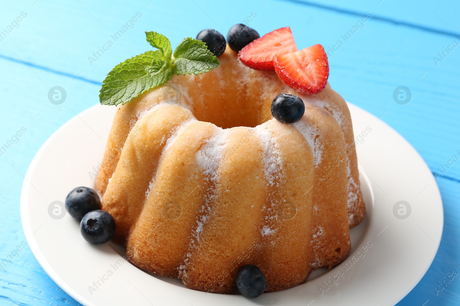 Tasty Bundt cake with powdered sugar and berries on light blue wooden table, closeup Photo of Tasty Bundt cake with powdered sugar and berries on light blue wooden table, closeup
