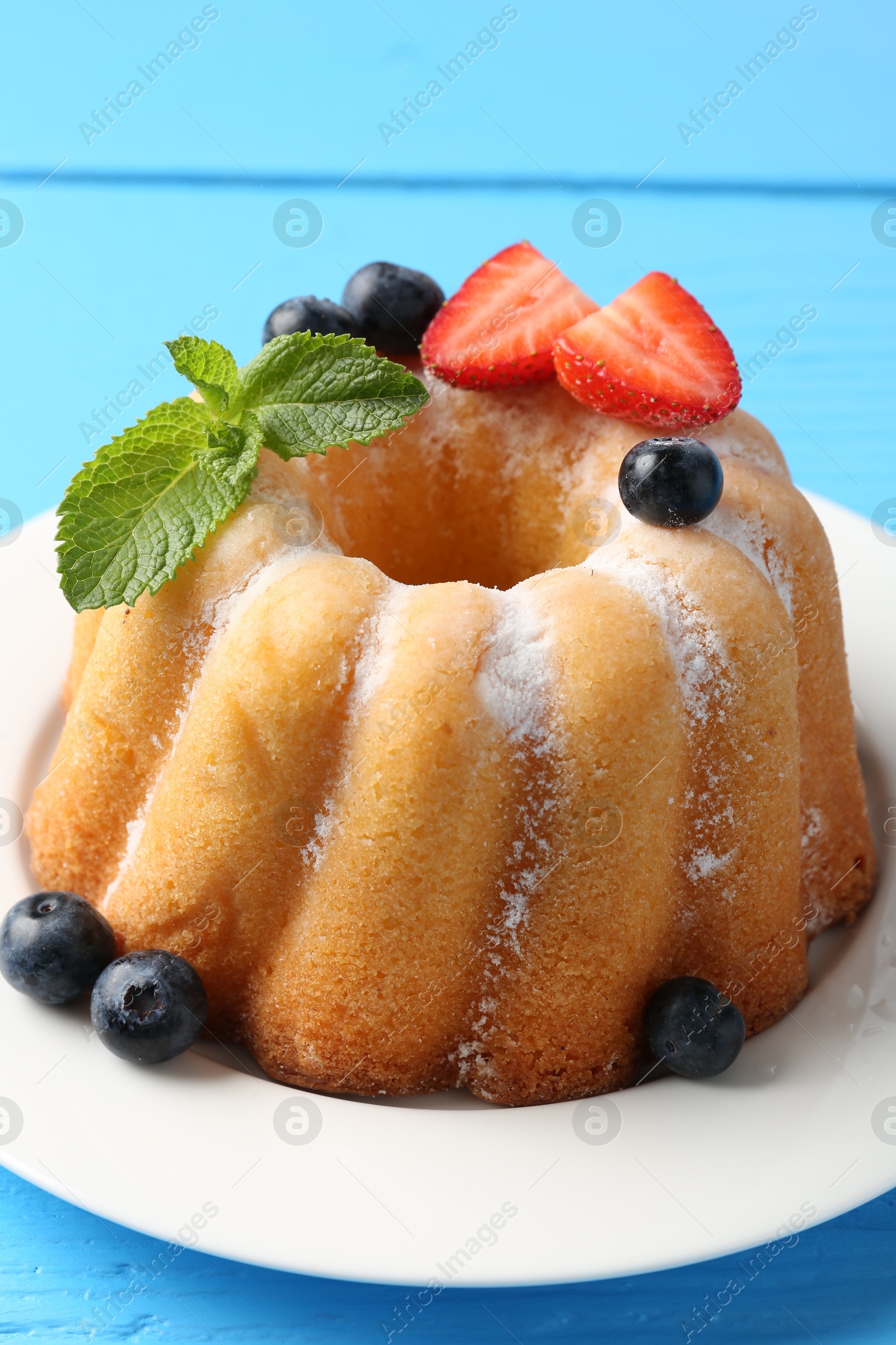 Tasty Bundt cake with powdered sugar and berries on light blue wooden table, closeup Photo of Tasty Bundt cake with powdered sugar and berries on light blue wooden table, closeup