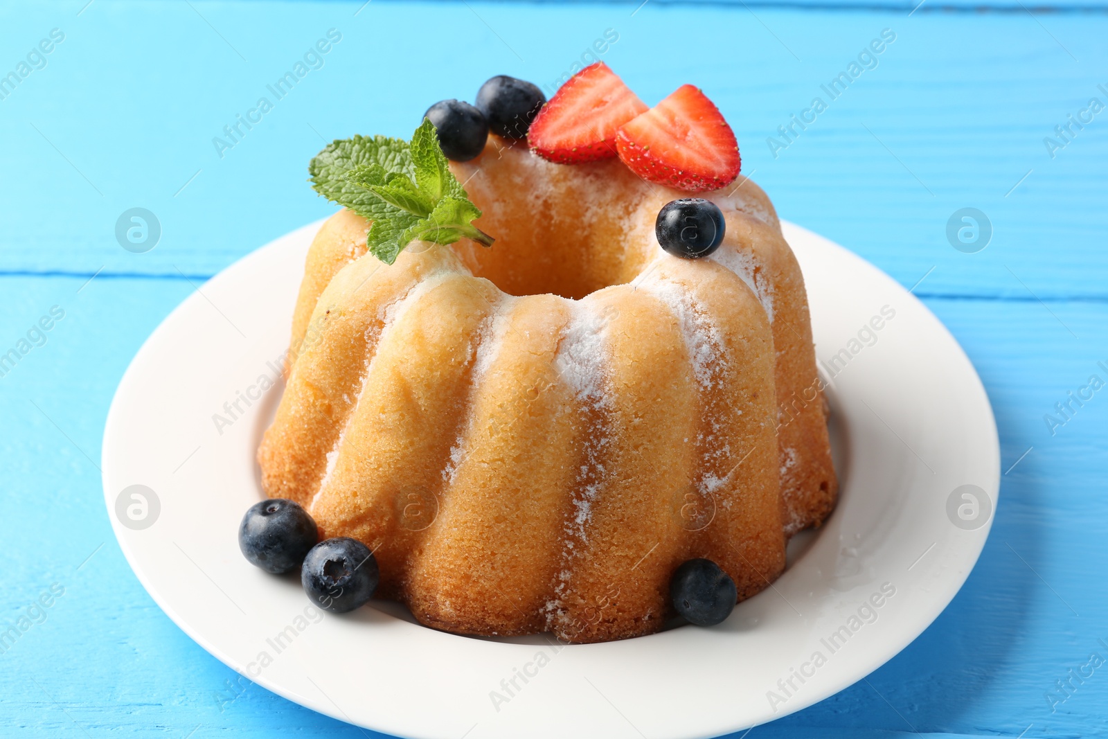 Tasty Bundt cake with powdered sugar and berries on light blue wooden table, closeup Photo of Tasty Bundt cake with powdered sugar and berries on light blue wooden table, closeup