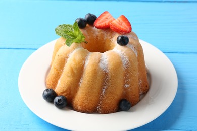 Photo of Tasty Bundt cake with powdered sugar and berries on light blue wooden table, closeup