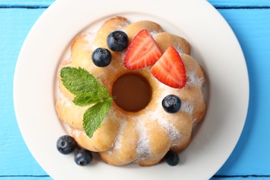 Photo of Tasty Bundt cake with powdered sugar and berries on light blue wooden table, top view