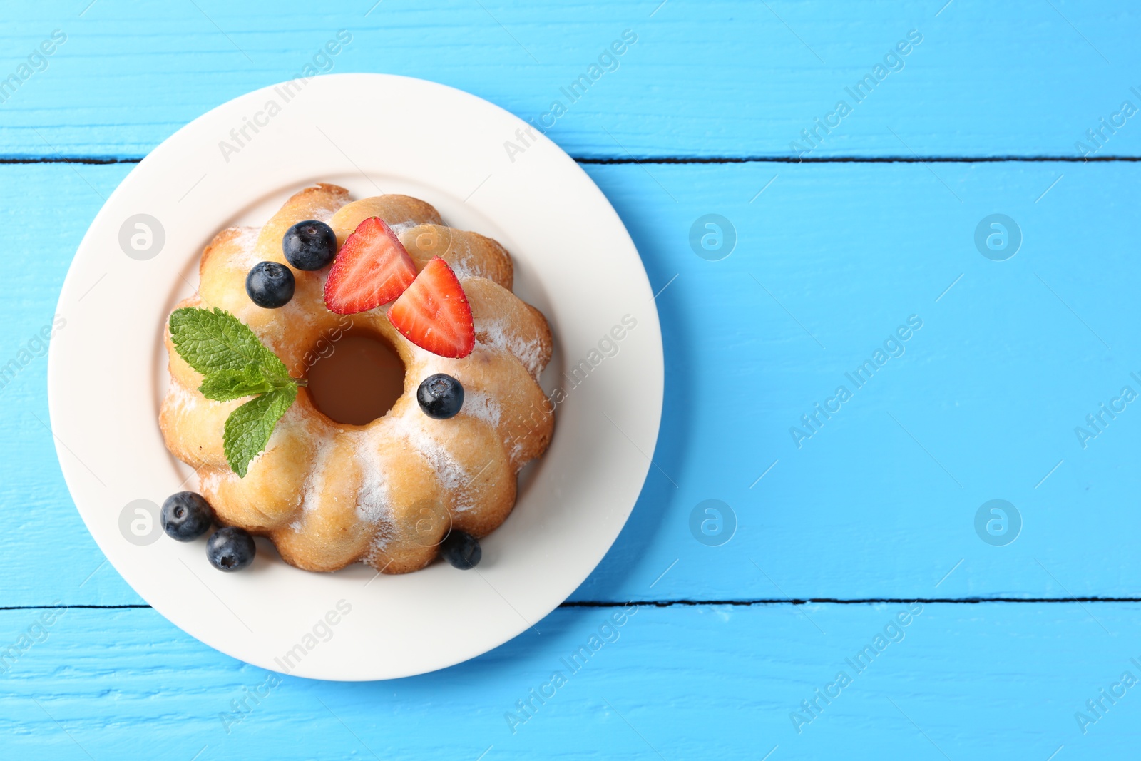 Tasty Bundt cake with powdered sugar and berries on light blue wooden table, top view. Space for text Photo of Tasty Bundt cake with powdered sugar and berries on light blue wooden table, top view. Space for text