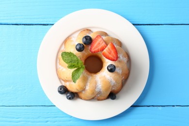 Photo of Tasty Bundt cake with powdered sugar and berries on light blue wooden table, top view