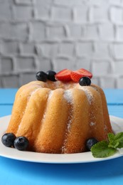 Photo of Tasty Bundt cake with powdered sugar and berries on light blue wooden table, closeup. Space for text