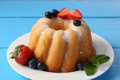 Photo of Tasty Bundt cake with powdered sugar and berries on light blue wooden table, closeup