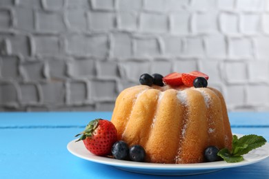 Photo of Tasty Bundt cake with powdered sugar and berries on light blue wooden table, closeup. Space for text