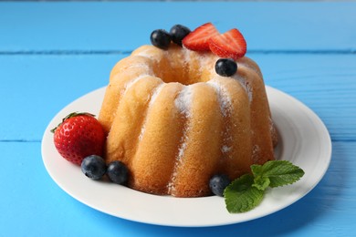 Photo of Tasty Bundt cake with powdered sugar and berries on light blue wooden table, closeup