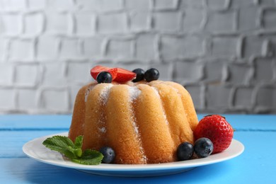 Photo of Tasty Bundt cake with powdered sugar and berries on light blue wooden table, closeup