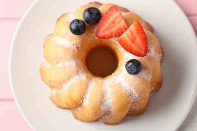 Photo of Tasty Bundt cake with powdered sugar and berries on pink wooden table, top view