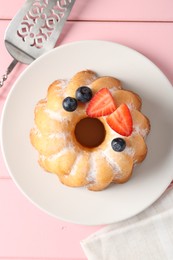 Photo of Tasty Bundt cake with powdered sugar, berries and server on pink wooden table, top view