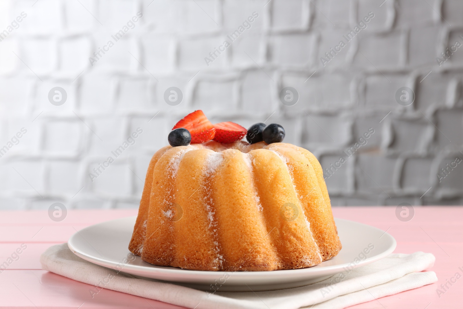 Tasty Bundt cake with powdered sugar and berries on pink wooden table, closeup Photo of Tasty Bundt cake with powdered sugar and berries on pink wooden table, closeup