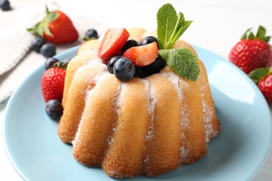 Photo of Tasty Bundt cake with powdered sugar and berries on white table, closeup