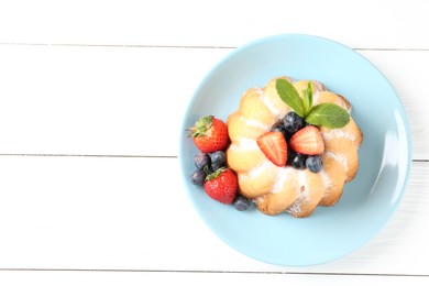 Photo of Tasty Bundt cake with powdered sugar and berries on white wooden table, top view. Space for text