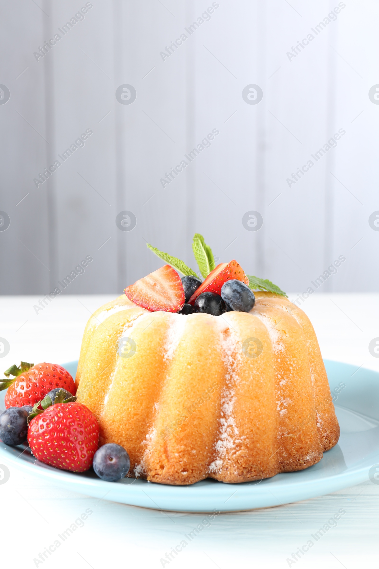 Tasty Bundt cake with powdered sugar and berries on white wooden table, closeup. Space for text Photo of Tasty Bundt cake with powdered sugar and berries on white wooden table, closeup. Space for text