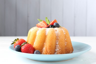 Photo of Tasty Bundt cake with powdered sugar and berries on white wooden table, closeup