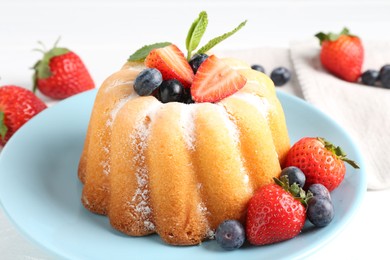 Photo of Tasty Bundt cake with powdered sugar and berries on white table, closeup