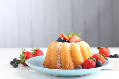 Photo of Tasty Bundt cake with powdered sugar and berries on white wooden table, closeup