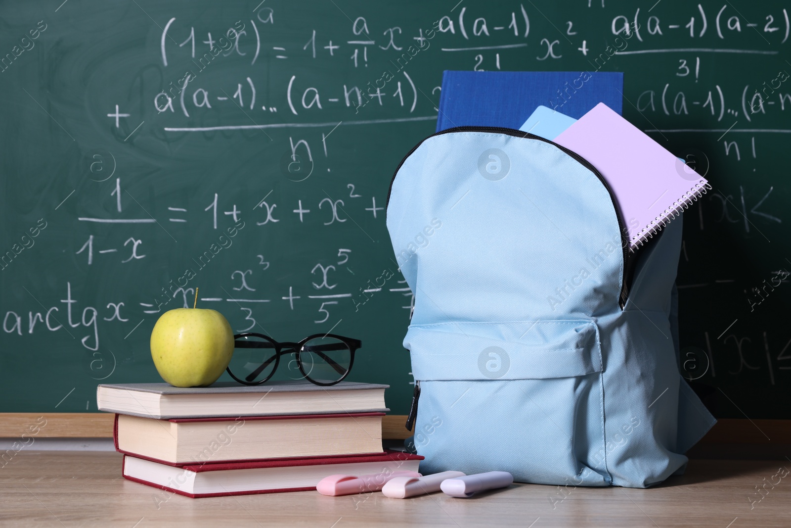 Backpack and books on wooden table near blackboard with formulas Photo of Backpack and books on wooden table near blackboard with formulas