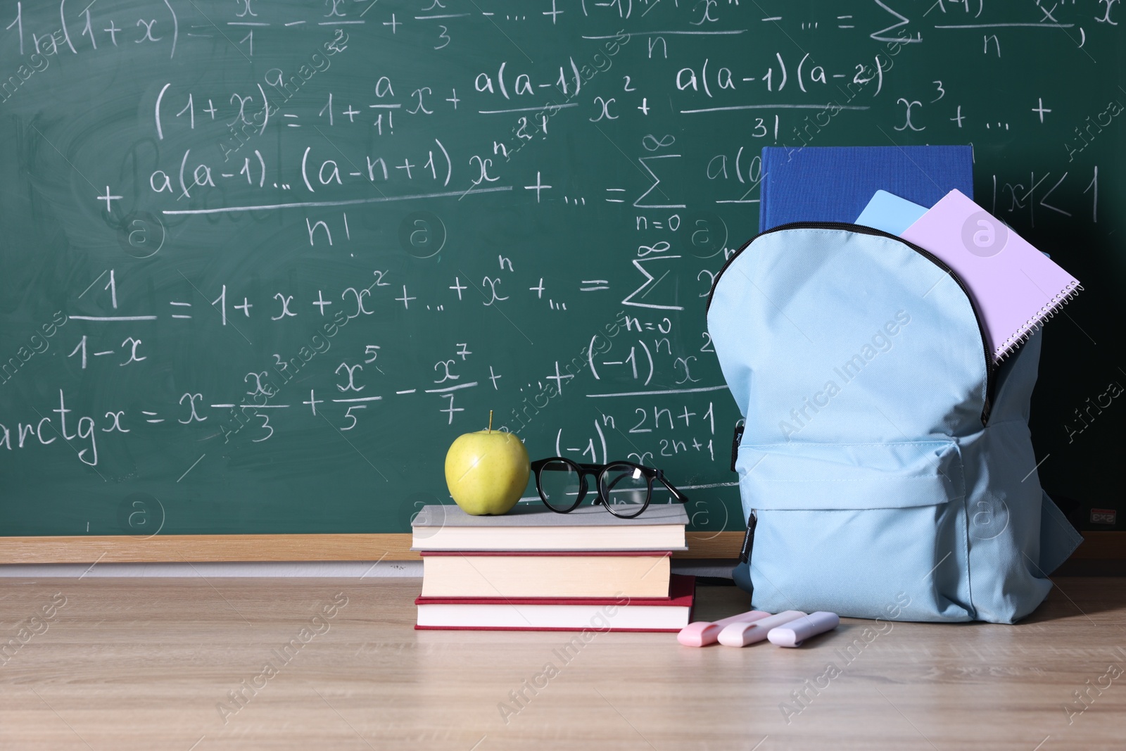 Backpack and books on wooden table near blackboard with formulas, space for text Photo of Backpack and books on wooden table near blackboard with formulas, space for text