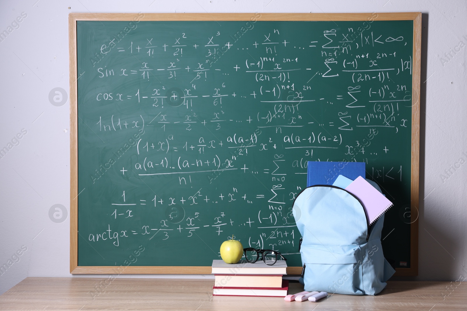 Backpack and books on wooden table near blackboard with formulas Photo of Backpack and books on wooden table near blackboard with formulas