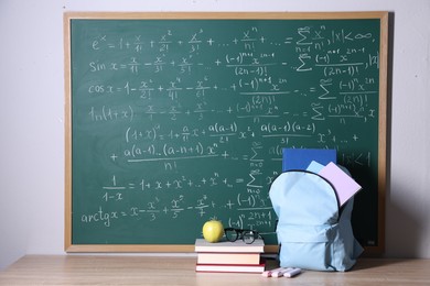 Photo of Backpack and books on wooden table near blackboard with formulas