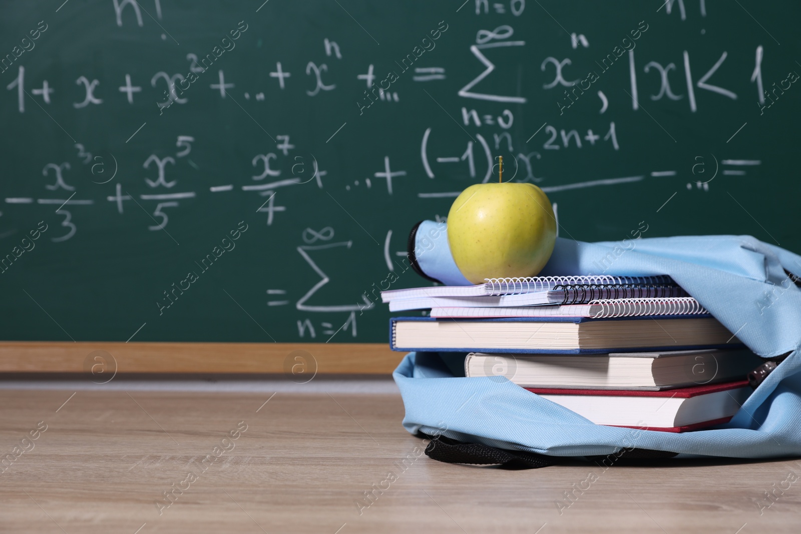 Backpack, apple and books on wooden table near blackboard with formulas, closeup. Space for text Photo of Backpack, apple and books on wooden table near blackboard with formulas, closeup. Space for text