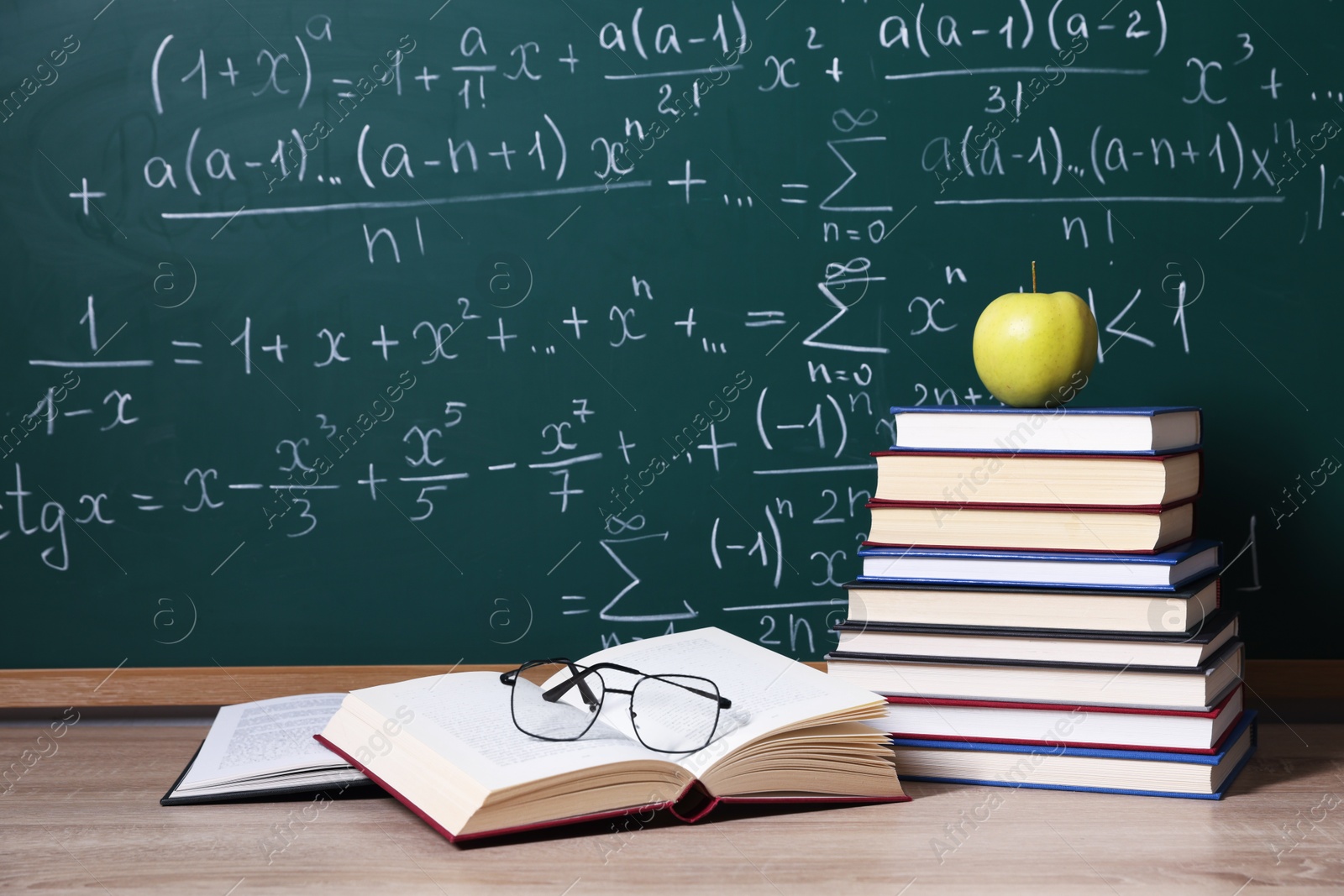 Books, glasses and apple on wooden table near blackboard with formulas Photo of Books, glasses and apple on wooden table near blackboard with formulas