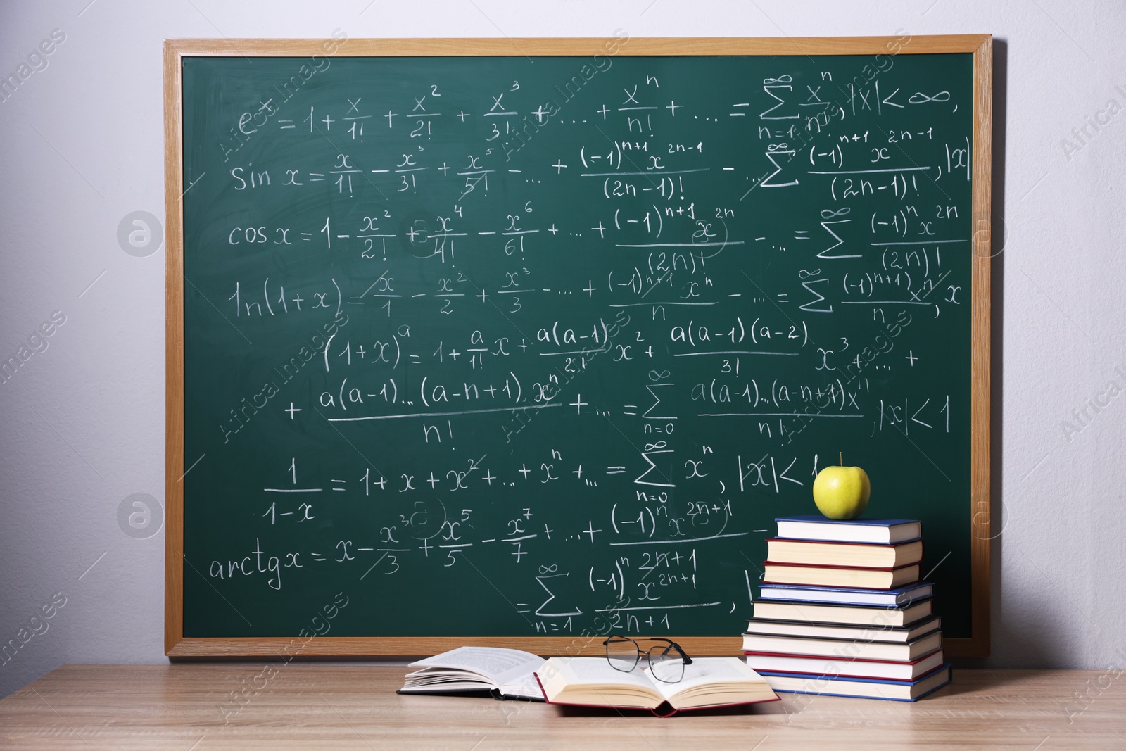 Books, glasses and apple on wooden table near blackboard with formulas Photo of Books, glasses and apple on wooden table near blackboard with formulas