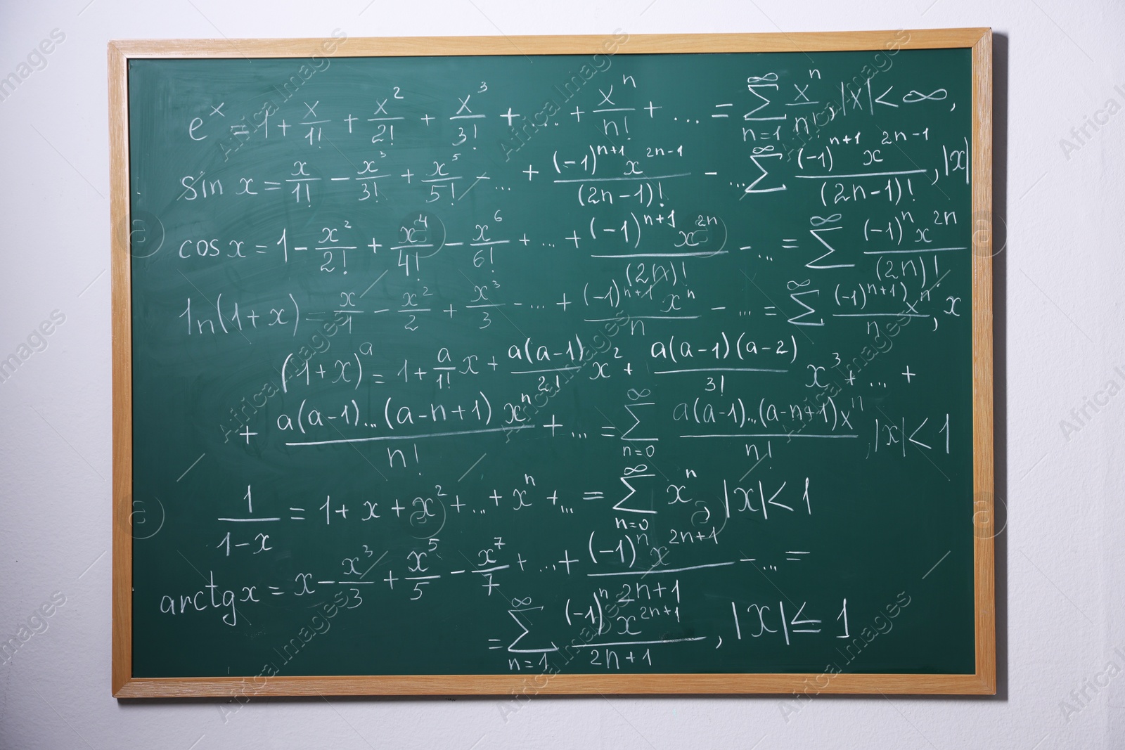 Different formulas written with chalk on blackboard on light grey wall Photo of Different formulas written with chalk on blackboard on light grey wall