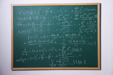 Photo of Different formulas written with chalk on blackboard on light grey wall