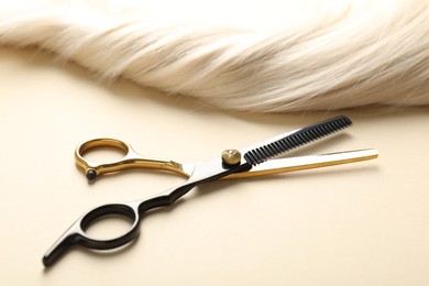 Photo of Hair lock and scissors on beige background, closeup