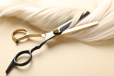 Photo of Hair lock and scissors on beige background, closeup