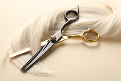 Photo of Hair lock and scissors on beige background, closeup