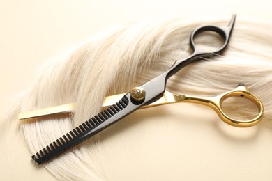 Photo of Hair lock and scissors on beige background, closeup