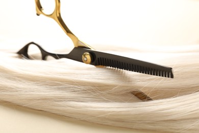 Photo of Hair lock and scissors on beige background, closeup