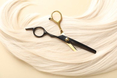 Photo of Hair lock and scissors on beige background, top view