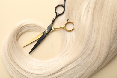 Photo of Hair lock and scissors on beige background, top view