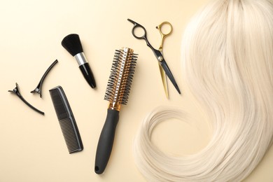 Photo of Hair lock and different hairdresser's tools on beige background, flat lay