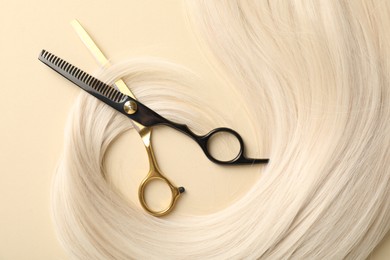 Photo of Hair lock and scissors on beige background, flat lay