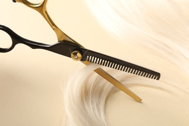 Photo of Hair lock and scissors on beige background, closeup