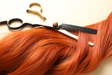 Photo of Hair lock and scissors on beige background, closeup