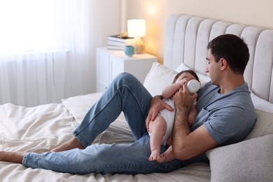 Photo of Father feeding his little baby with bottle on bed at home. Space for text