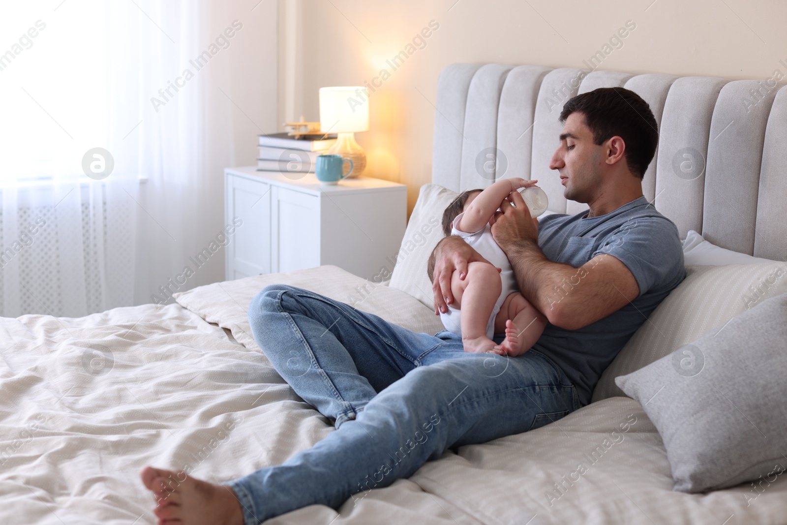 Father feeding his little baby with bottle on bed at home. Space for text Photo of Father feeding his little baby with bottle on bed at home. Space for text