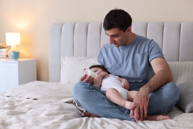 Photo of Father feeding his little baby with bottle on bed at home. Space for text