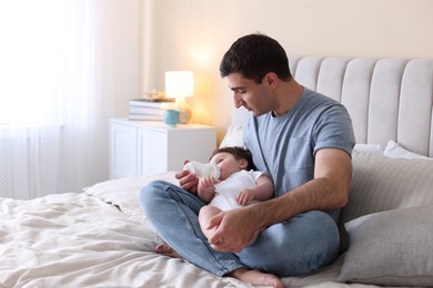 Photo of Father feeding his little baby with bottle on bed at home. Space for text